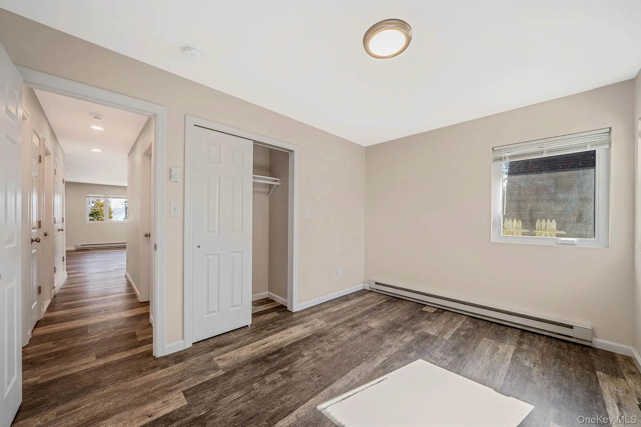 Unfurnished bedroom with baseboard heating, a closet, and dark wood-style flooring Unfurnished bedroom with baseboard heating, a closet, and dark wood-style flooring