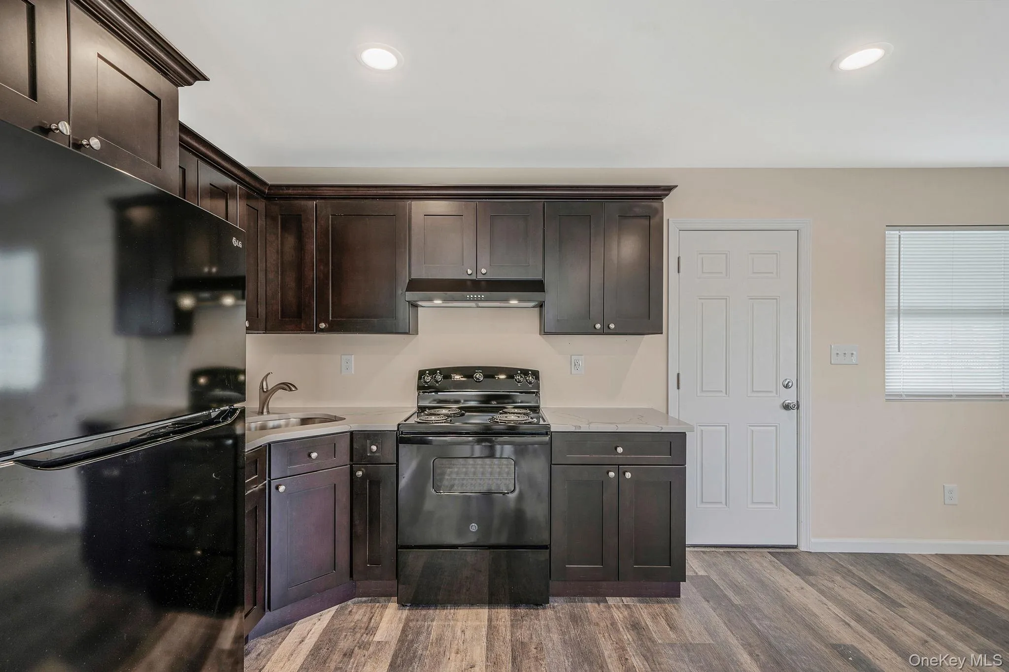 Kitchen featuring black appliances, dark brown cabinets, under cabinet range hood, dark wood-style floors, and recessed lighting Kitchen featuring black appliances, dark brown cabinets, under cabinet range hood, dark wood-style floors, and recessed lighting