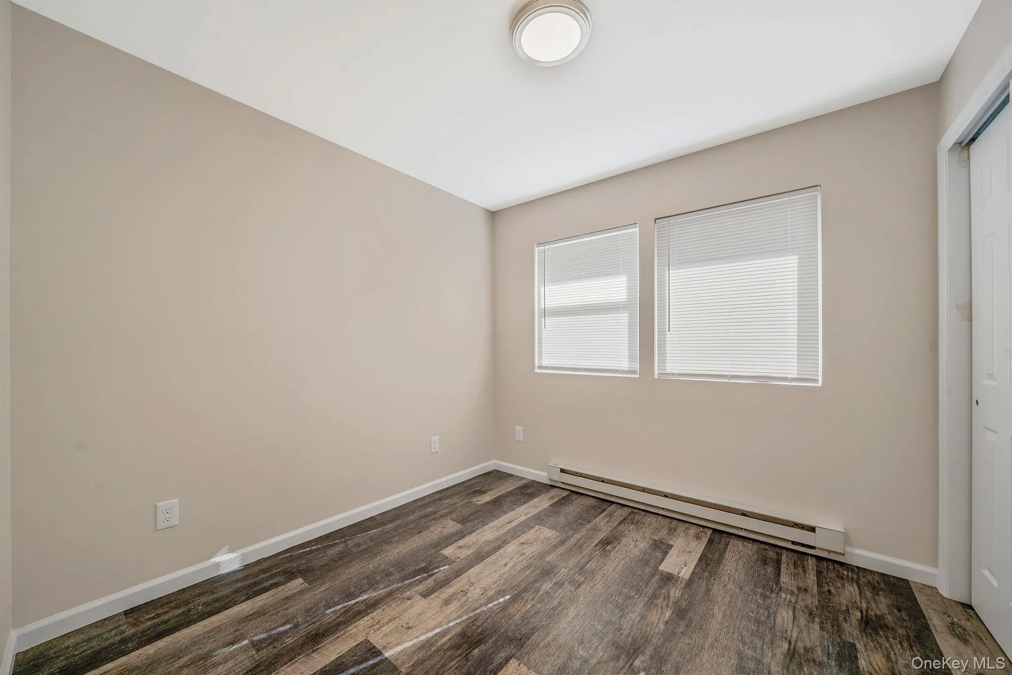 Unfurnished bedroom featuring a baseboard heating unit, dark wood-type flooring, and a closet Unfurnished bedroom featuring a baseboard heating unit, dark wood-type flooring, and a closet