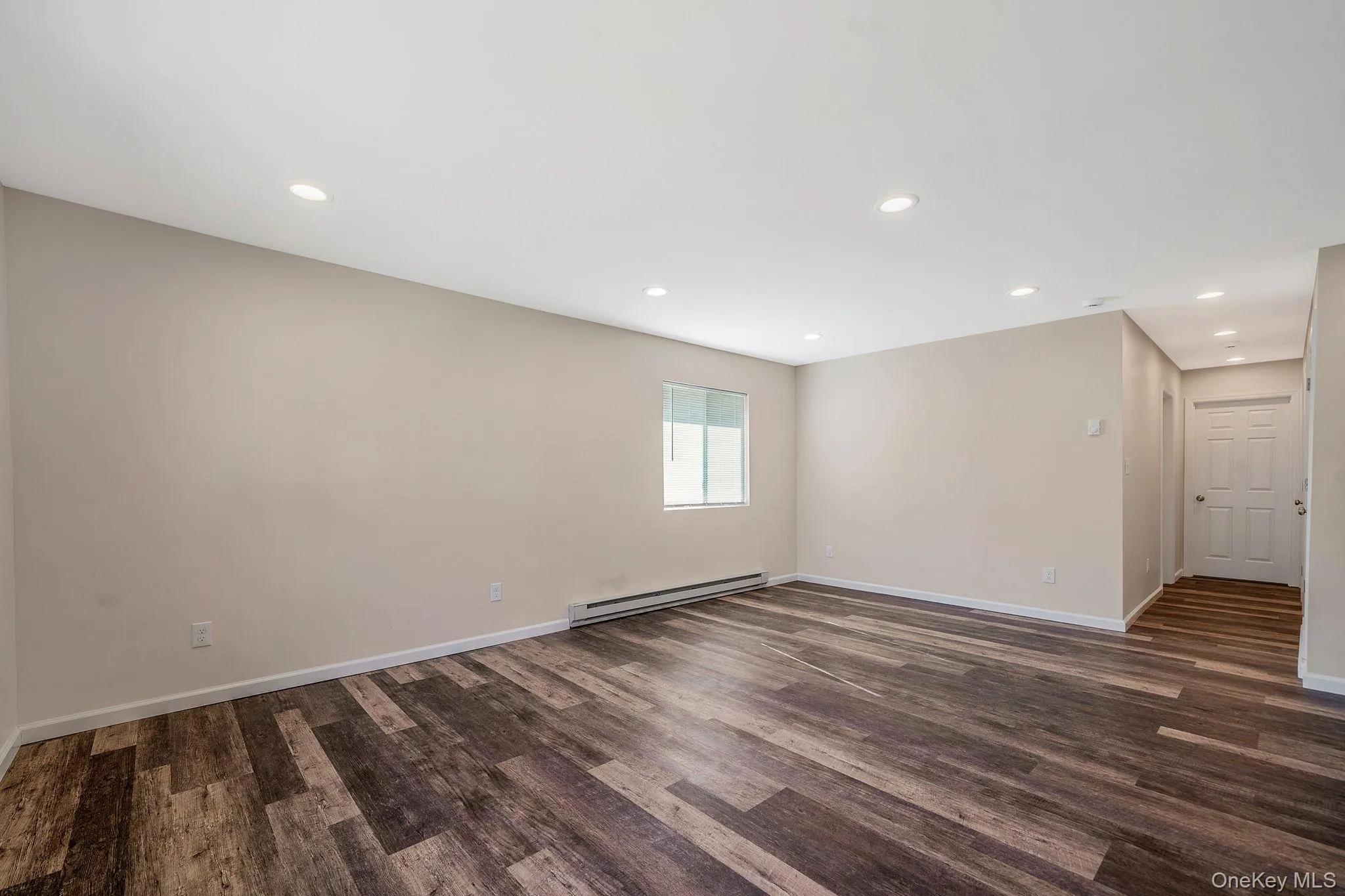 Empty room featuring baseboard heating, recessed lighting, and dark wood finished floors Empty room featuring baseboard heating, recessed lighting, and dark wood finished floors