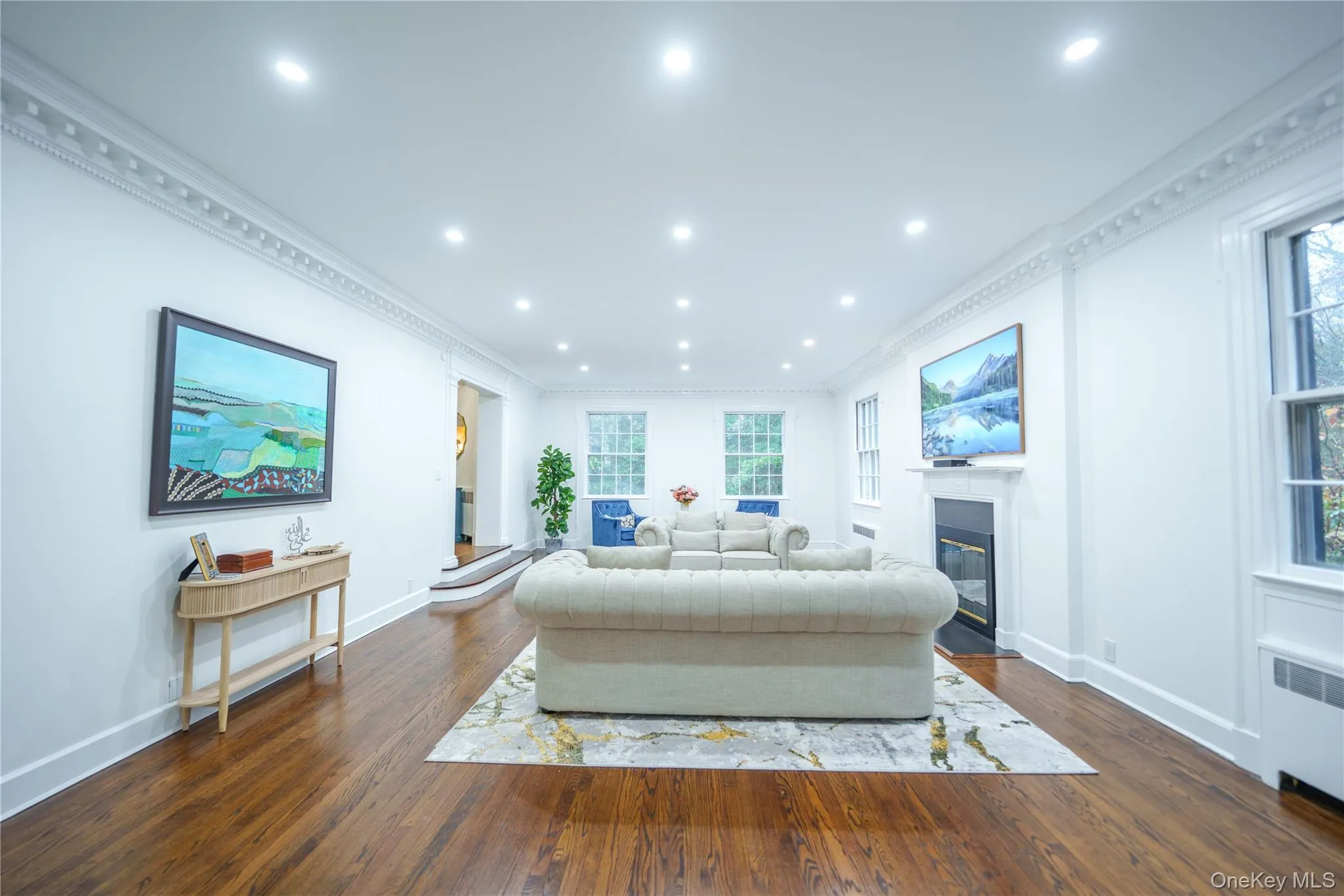 Living area featuring crown molding, dark wood-style floors, a fireplace with flush hearth, recessed lighting, and radiator Living area featuring crown molding, dark wood-style floors, a fireplace with flush hearth, recessed lighting, and radiator