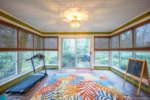 Solarium featuring baseboard heating, a chandelier, ornamental moldings & sliders to bluestone patio Solarium featuring baseboard heating, a chandelier, ornamental moldings & sliders to bluestone patio