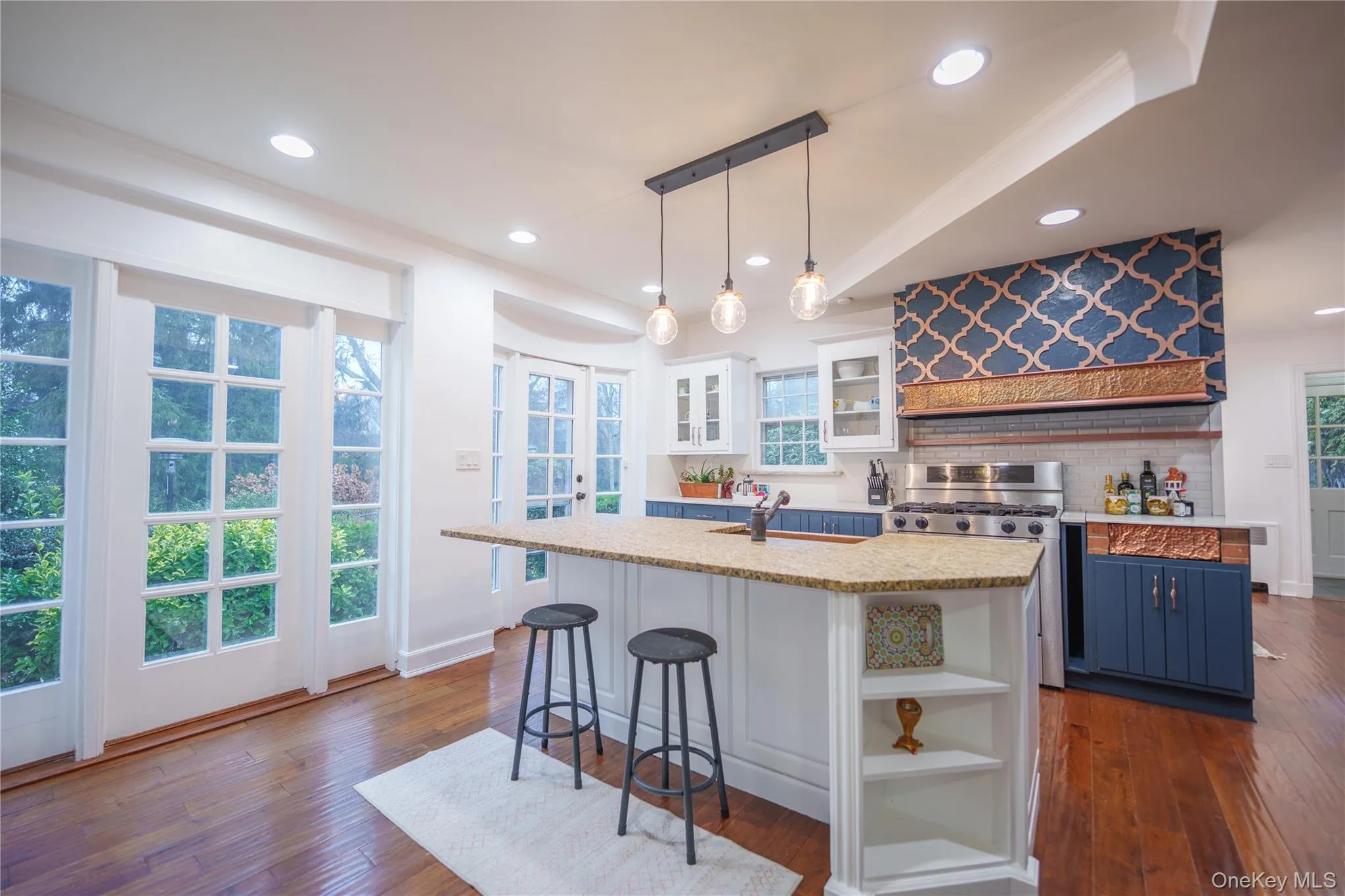 Kitchen featuring white cabinetry, open shelves, hanging light fixtures, a breakfast bar, and an island with sink Kitchen featuring white cabinetry, open shelves, hanging light fixtures, a breakfast bar, and an island with sink