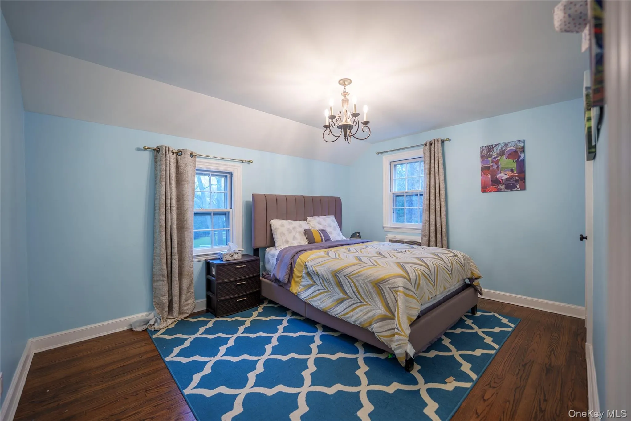 Opposite of Blue Carped bedroom is this bedroom with lofted ceiling, multiple windows, dark wood flooring, and a chandelier Opposite of Blue Carped bedroom is this bedroom with lofted ceiling, multiple windows, dark wood flooring, and a chandelier