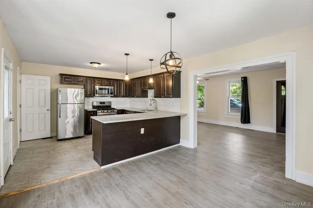 Kitchen with dark brown cabinets, stainless steel appliances, hanging light fixtures, and light wood-type flooring Kitchen with dark brown cabinets, stainless steel appliances, hanging light fixtures, and light wood-type flooring