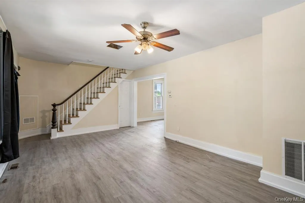 Unfurnished living room with stairway, light wood-style flooring, and a ceiling fan Unfurnished living room with stairway, light wood-style flooring, and a ceiling fan