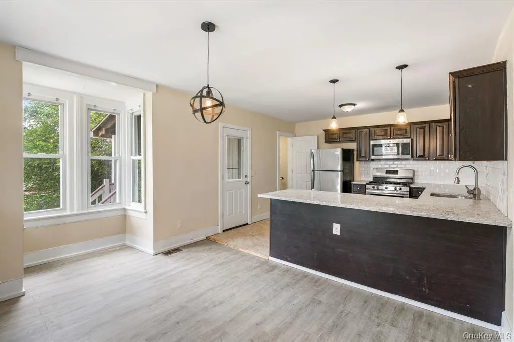 Kitchen featuring dark brown cabinetry, a peninsula, light stone countertops, stainless steel appliances, and decorative light fixtures Kitchen featuring dark brown cabinetry, a peninsula, light stone countertops, stainless steel appliances, and decorative light fixtures