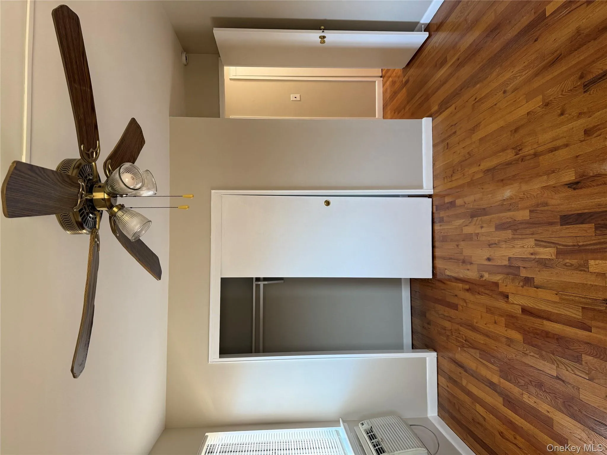 Unfurnished bedroom with dark wood-style floors, ceiling fan, a closet, and an AC wall unit Unfurnished bedroom with dark wood-style floors, ceiling fan, a closet, and an AC wall unit