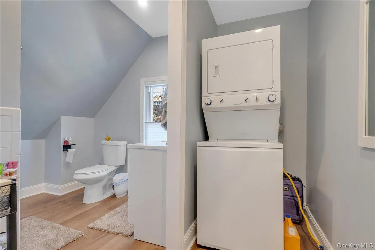 Laundry area featuring stacked washer / dryer, light wood-style flooring, and vaulted ceiling Laundry area featuring stacked washer / dryer, light wood-style flooring, and vaulted ceiling