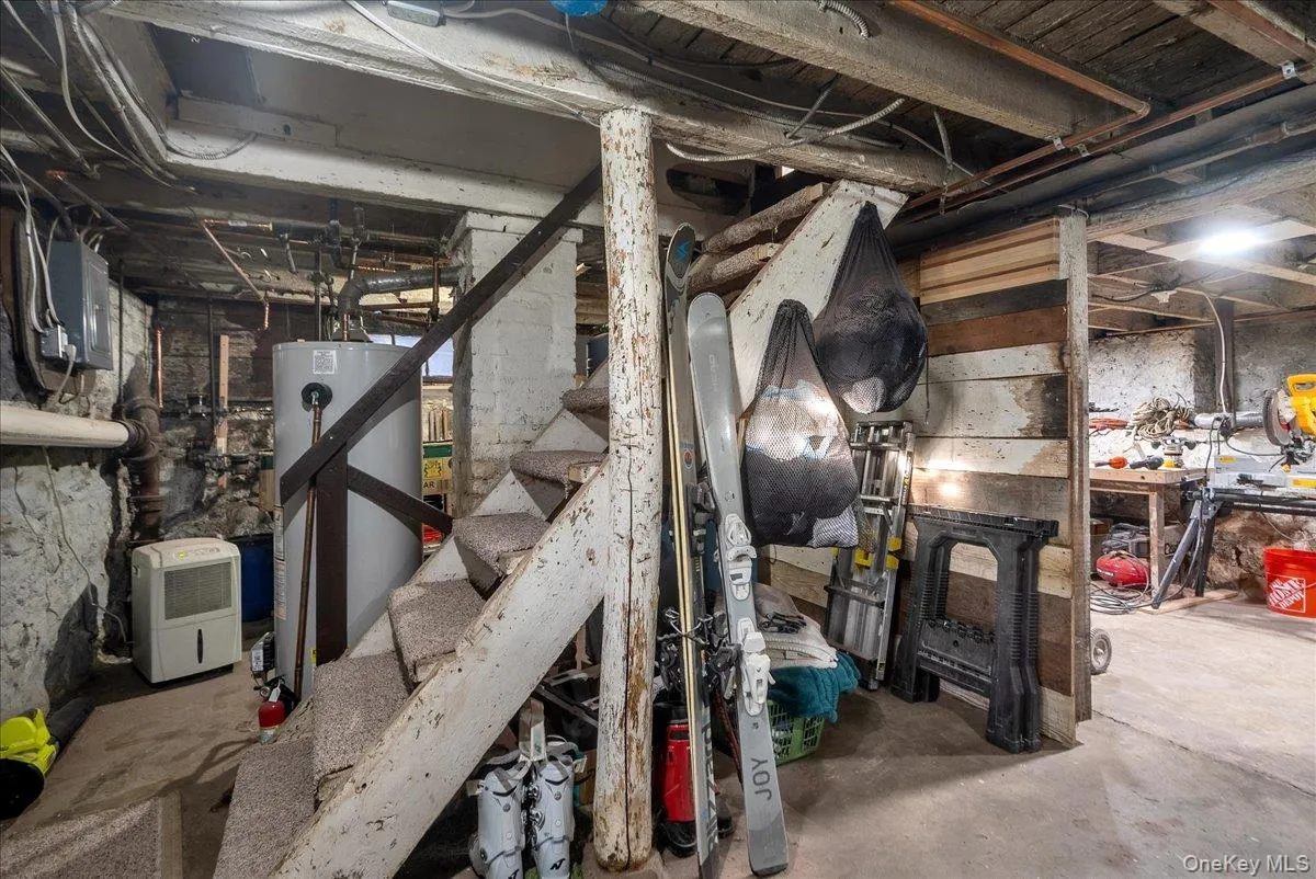 Unfinished below grade area featuring water heater, electric panel, and stairs Unfinished below grade area featuring water heater, electric panel, and stairs