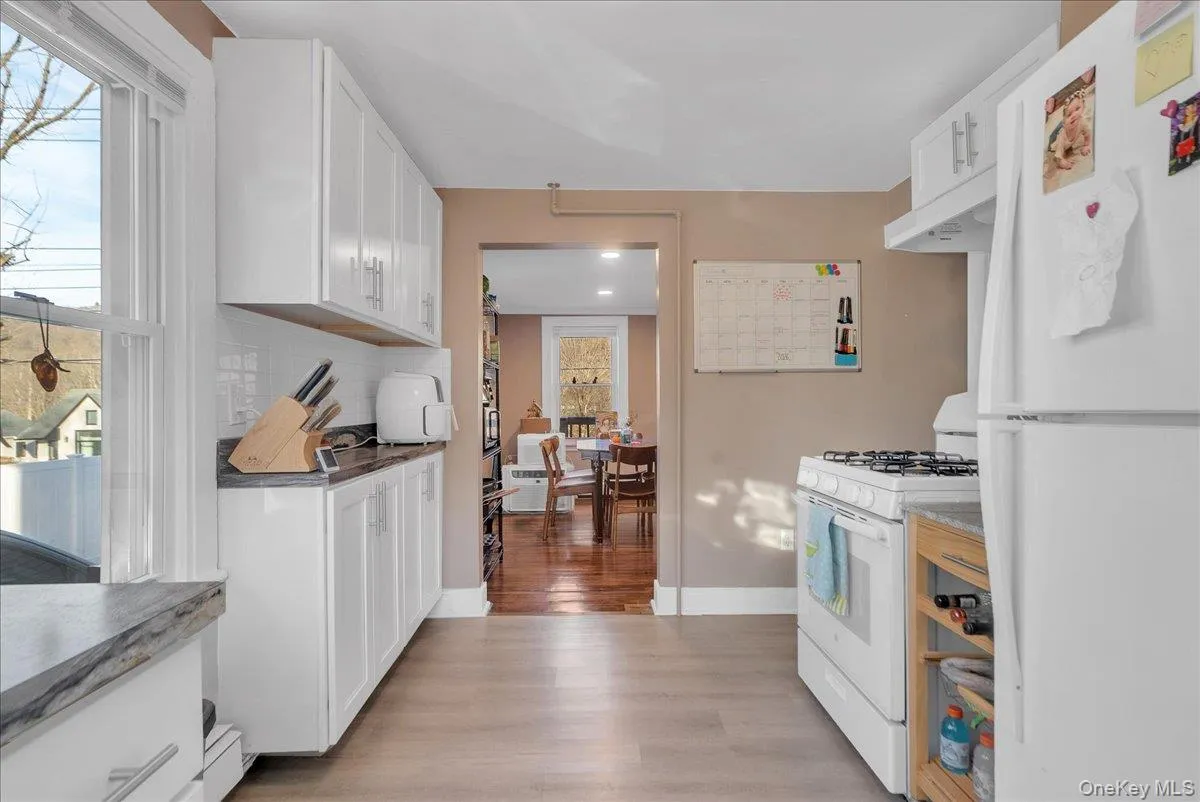 Kitchen with white appliances, white cabinets, light wood-style flooring, under cabinet range hood, and tasteful backsplash Kitchen with white appliances, white cabinets, light wood-style flooring, under cabinet range hood, and tasteful backsplash