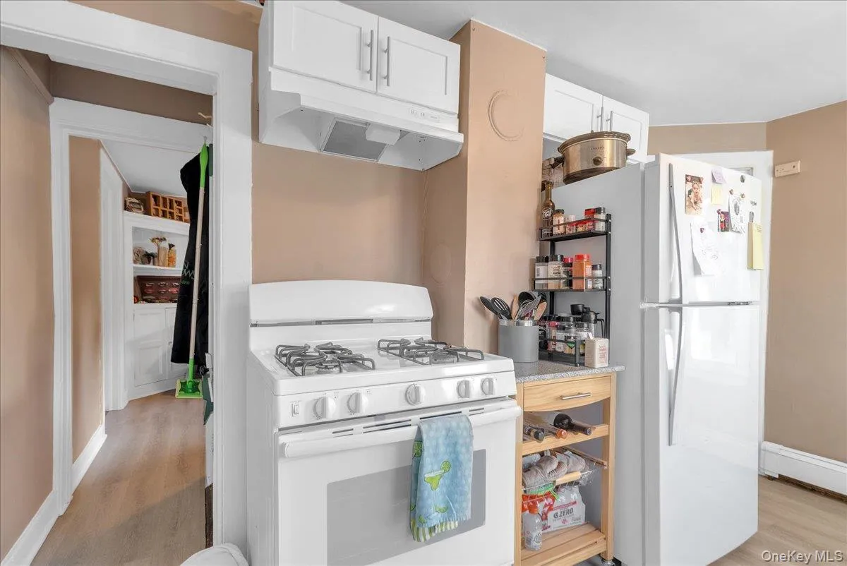 Kitchen featuring white appliances, light wood finished floors, under cabinet range hood, and white cabinetry Kitchen featuring white appliances, light wood finished floors, under cabinet range hood, and white cabinetry