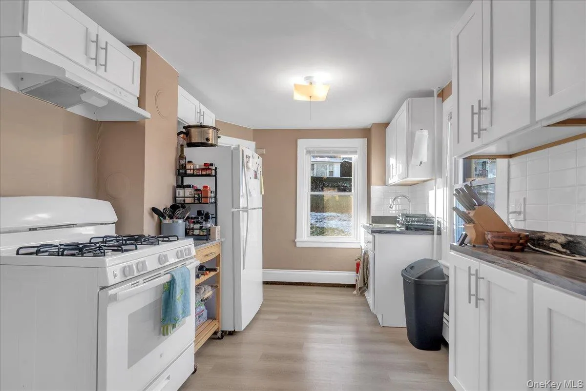 Kitchen featuring white appliances, backsplash, white cabinetry, and light wood-style floors Kitchen featuring white appliances, backsplash, white cabinetry, and light wood-style floors