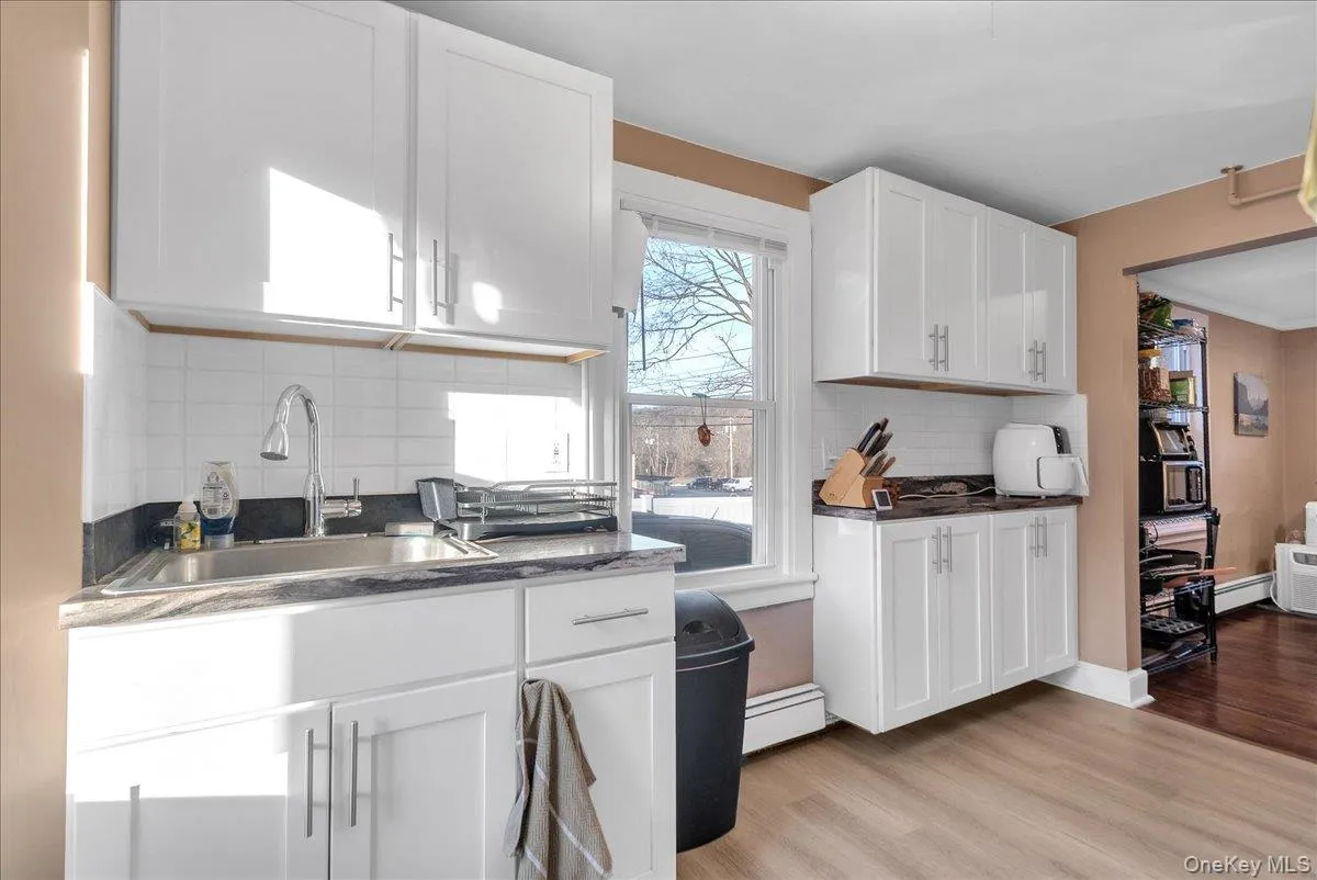 Kitchen featuring white cabinets, light wood-style flooring, decorative backsplash, dark stone counters, and a baseboard heating unit Kitchen featuring white cabinets, light wood-style flooring, decorative backsplash, dark stone counters, and a baseboard heating unit