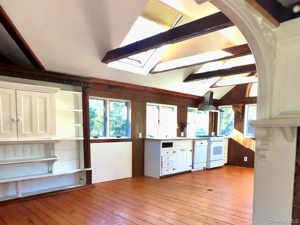 Kitchen with white cabinetry, white appliances, island exhaust hood, light wood finished floors, and a skylight Kitchen with white cabinetry, white appliances, island exhaust hood, light wood finished floors, and a skylight