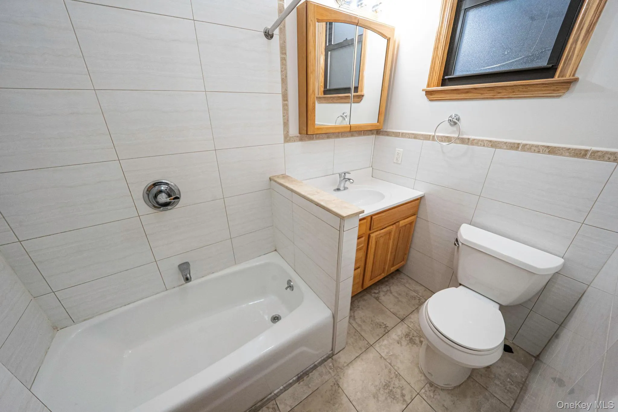 Bathroom with shower / tub combination, vanity, tile walls, and light tile patterned flooring Bathroom with shower / tub combination, vanity, tile walls, and light tile patterned flooring