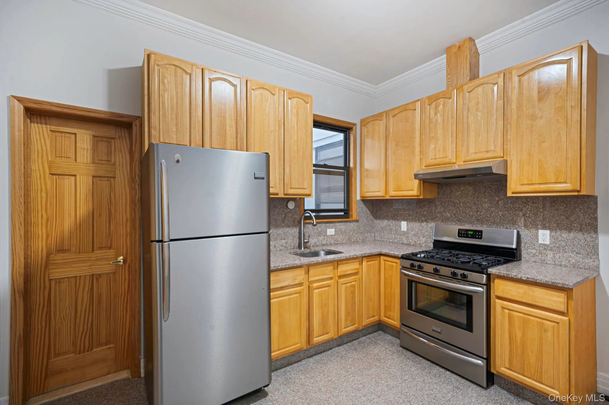 Kitchen featuring stainless steel appliances, granite tiled floors, light stone counters, ornamental molding, and under cabinet range hood Kitchen featuring stainless steel appliances, granite tiled floors, light stone counters, ornamental molding, and under cabinet range hood