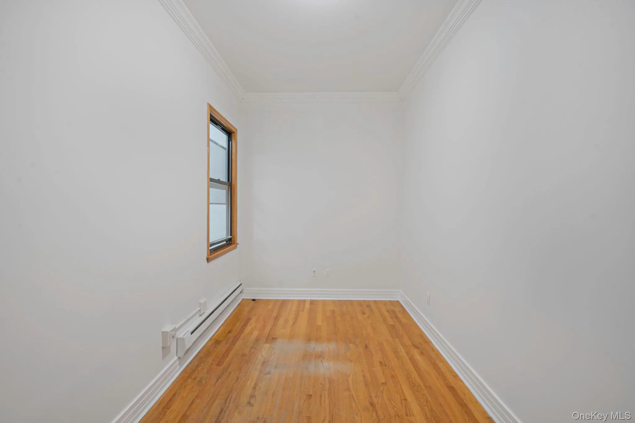 Unfurnished room with a baseboard radiator, ornamental molding, and light wood-style floors Unfurnished room with a baseboard radiator, ornamental molding, and light wood-style floors