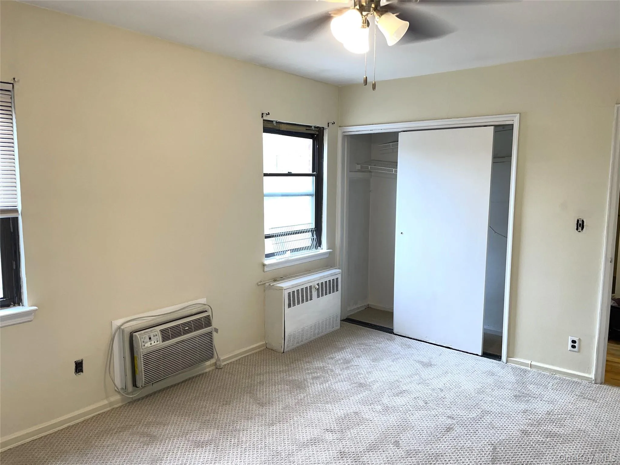 Unfurnished bedroom featuring light carpet, a closet, ceiling fan, radiator heating unit, and heating unit Unfurnished bedroom featuring light carpet, a closet, ceiling fan, radiator heating unit, and heating unit