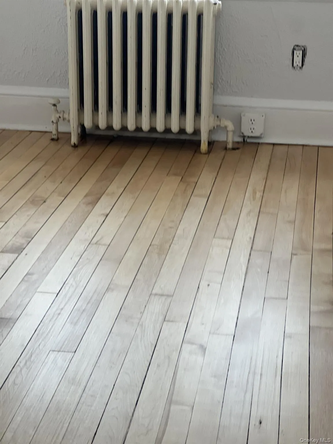 Detailed view of radiator, wood finished floors, and a textured wall Detailed view of radiator, wood finished floors, and a textured wall