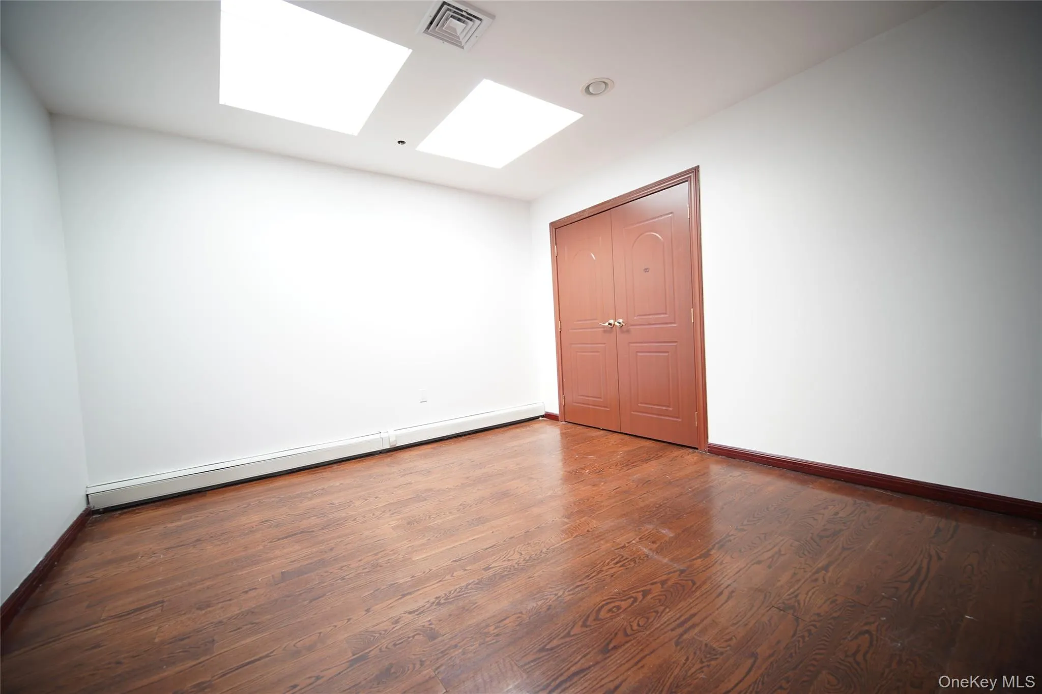 Empty room featuring a skylight, baseboard heating, and wood finished floors Empty room featuring a skylight, baseboard heating, and wood finished floors