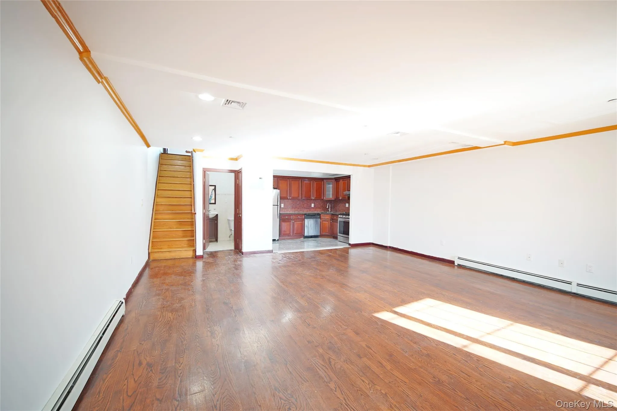 Unfurnished living room with a baseboard heating unit, stairway, ornamental molding, dark wood-type flooring, and recessed lighting Unfurnished living room with a baseboard heating unit, stairway, ornamental molding, dark wood-type flooring, and recessed lighting