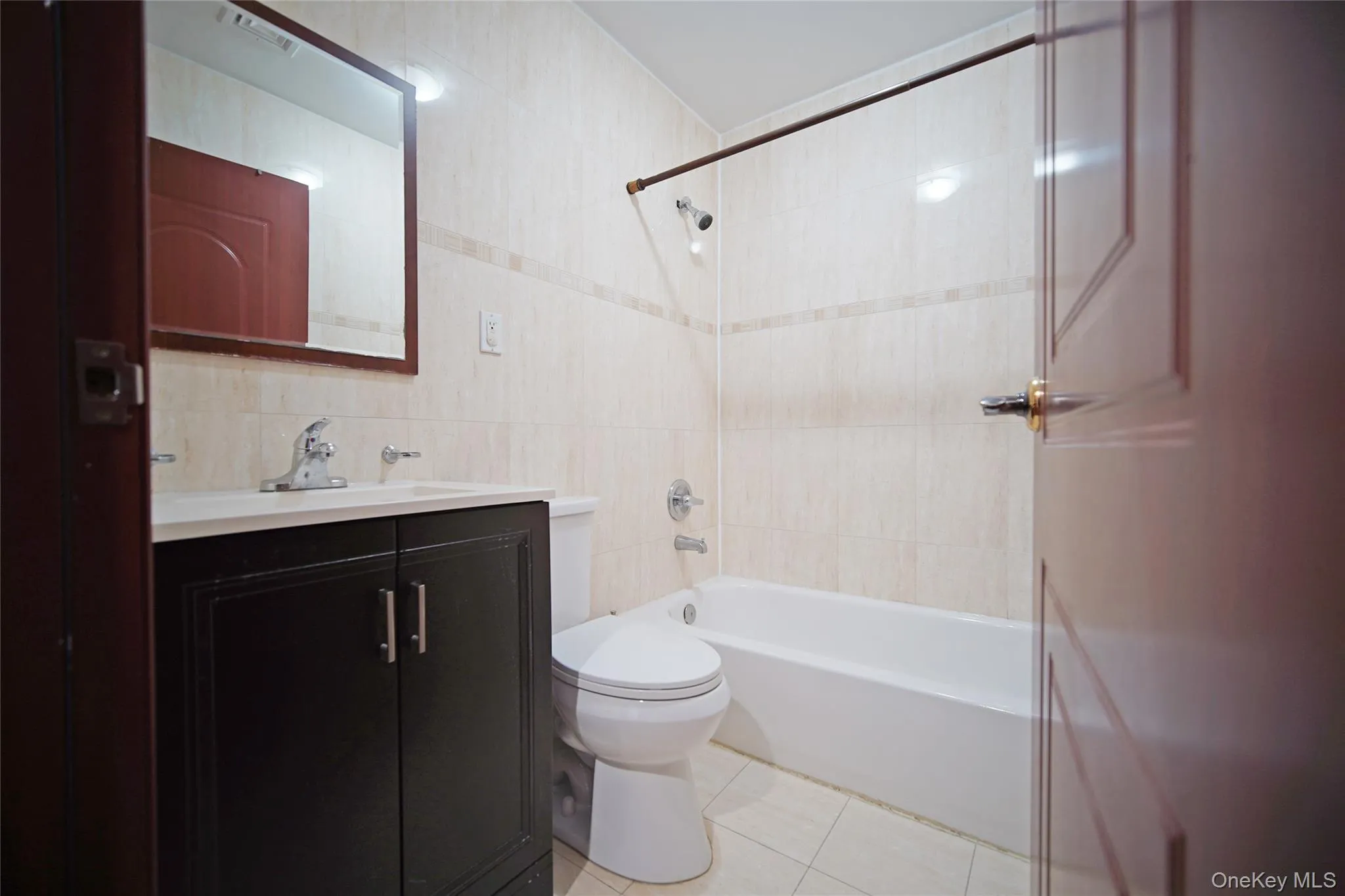 Bathroom featuring tile walls, vanity, bathtub / shower combination, and light tile patterned floors Bathroom featuring tile walls, vanity, bathtub / shower combination, and light tile patterned floors