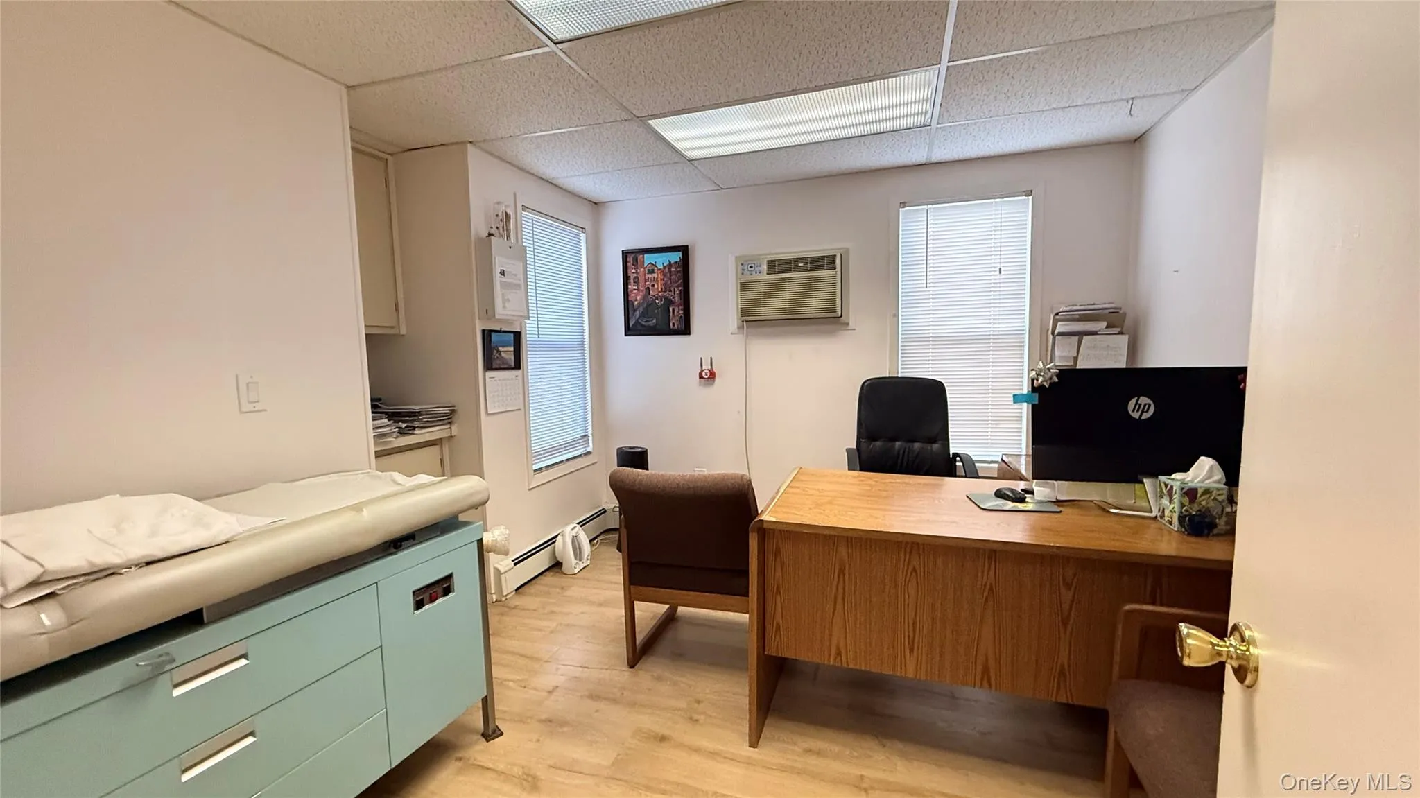 Office space featuring a paneled ceiling, light wood-style floors, baseboard heating, and a wall unit AC Office space featuring a paneled ceiling, light wood-style floors, baseboard heating, and a wall unit AC