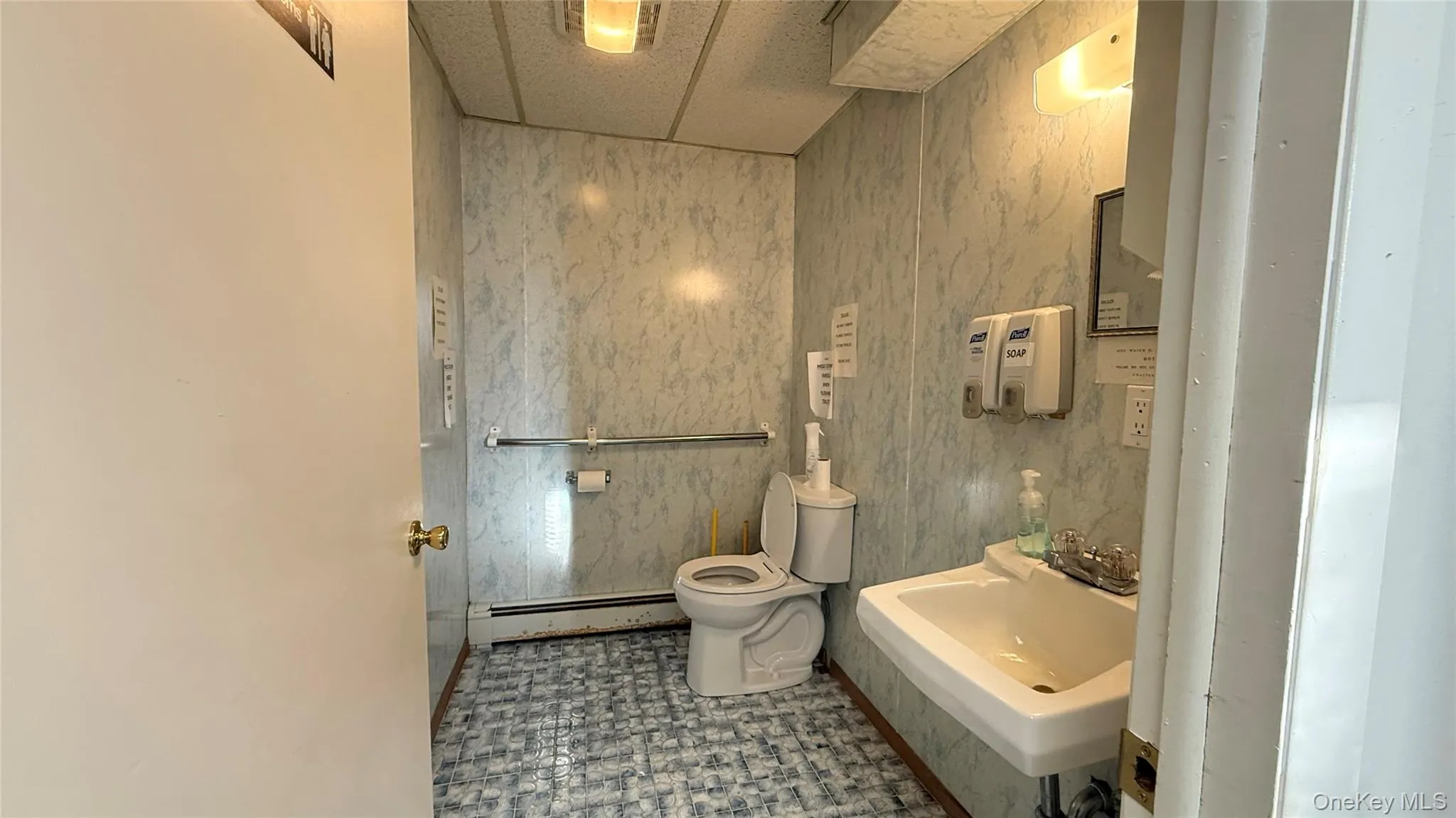 Half bath featuring tile patterned floors, baseboard heating, tile walls, and a drop ceiling Half bath featuring tile patterned floors, baseboard heating, tile walls, and a drop ceiling
