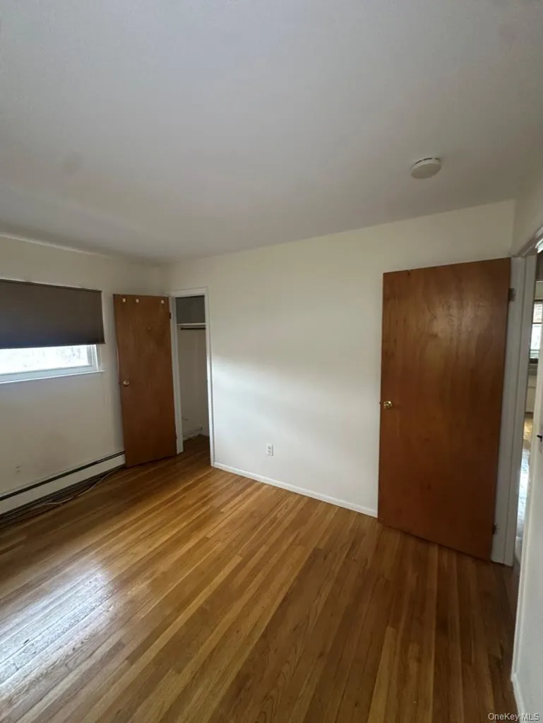 Unfurnished bedroom with hardwood / wood-style floors, baseboard heating, and a closet Unfurnished bedroom with hardwood / wood-style floors, baseboard heating, and a closet