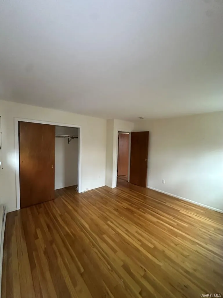 Unfurnished bedroom with hardwood / wood-style floors, a baseboard heating unit, and a closet Unfurnished bedroom with hardwood / wood-style floors, a baseboard heating unit, and a closet