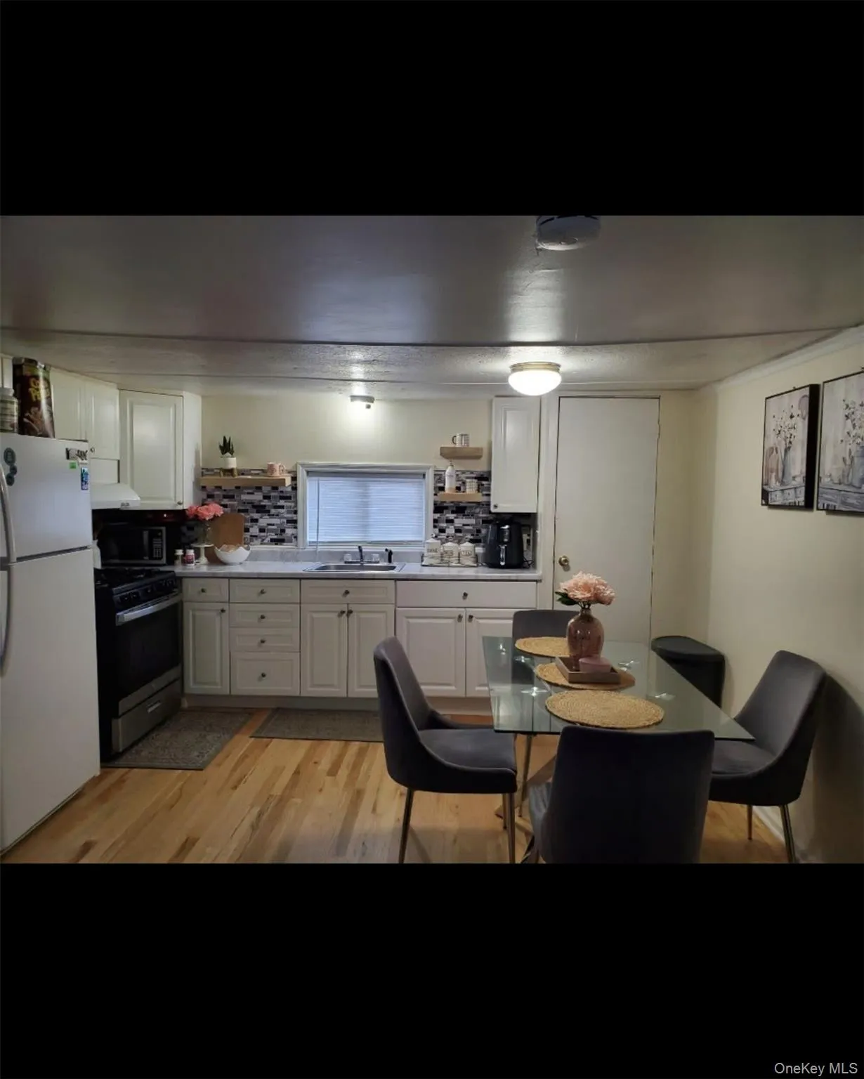 Kitchen with stainless steel appliances, backsplash, open shelves, white cabinets, and light wood finished floors Kitchen with stainless steel appliances, backsplash, open shelves, white cabinets, and light wood finished floors