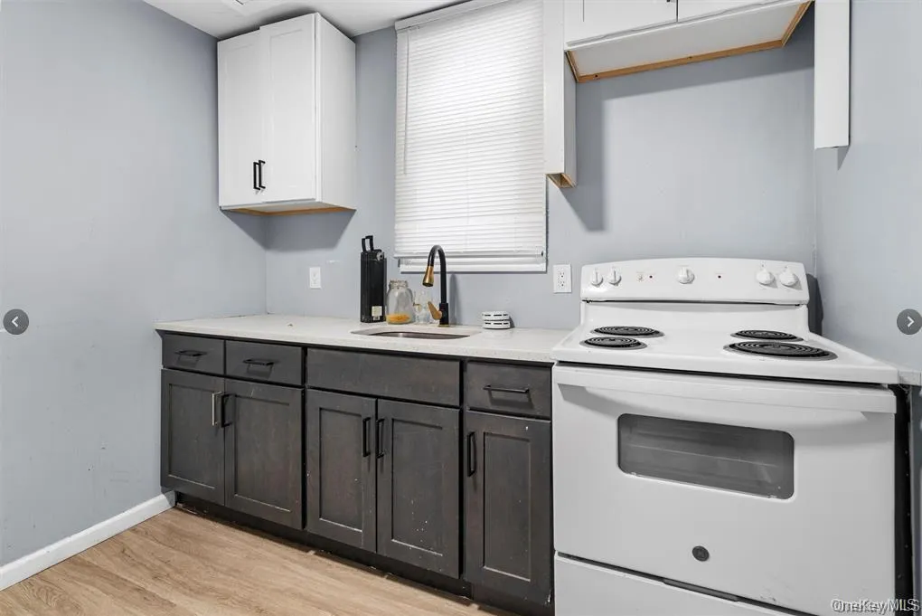 Kitchen with electric range, white cabinets, light wood-type flooring, and light stone countertops Kitchen with electric range, white cabinets, light wood-type flooring, and light stone countertops