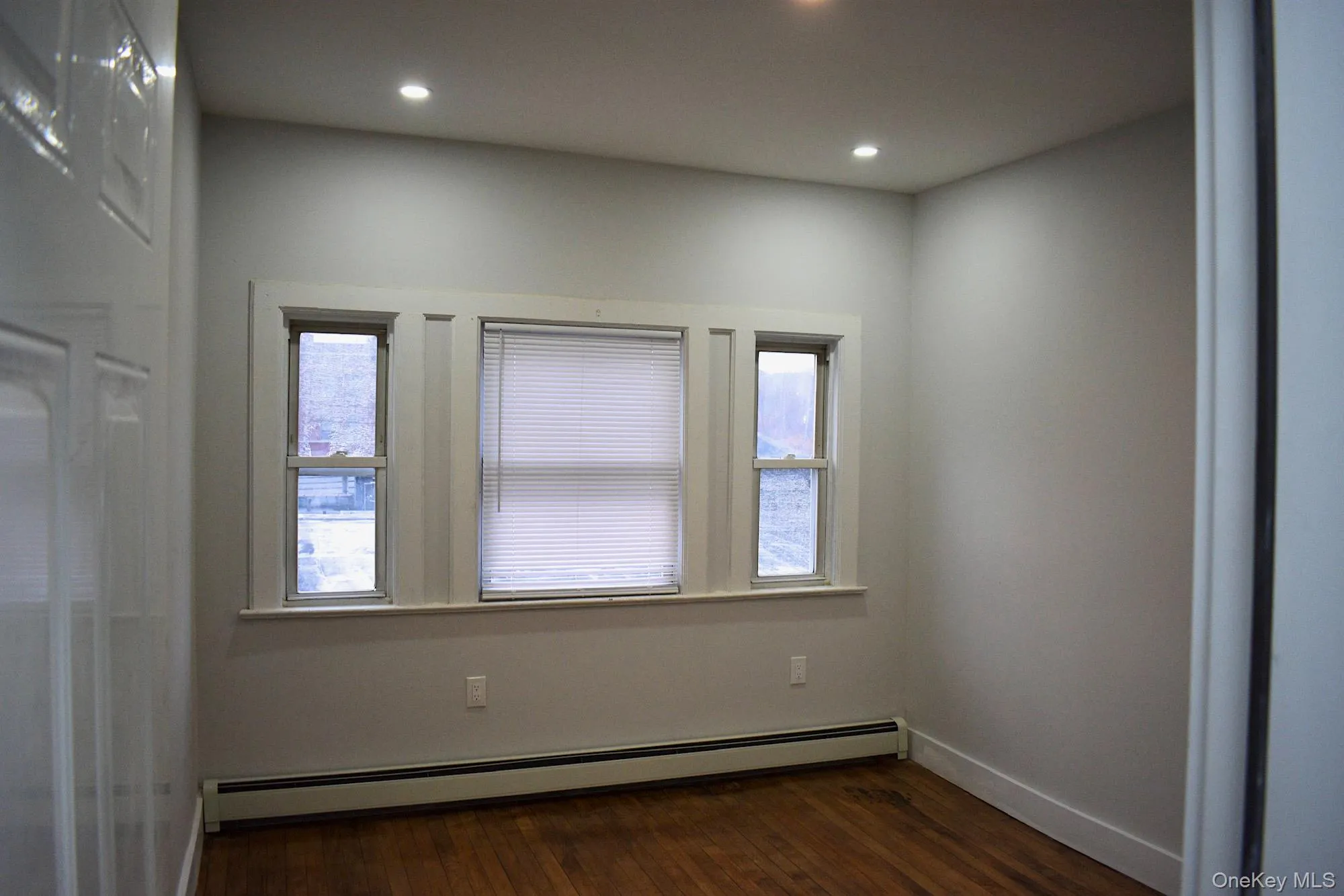 Empty room featuring a baseboard radiator, dark wood-style flooring, healthy amount of natural light, and recessed lighting Empty room featuring a baseboard radiator, dark wood-style flooring, healthy amount of natural light, and recessed lighting