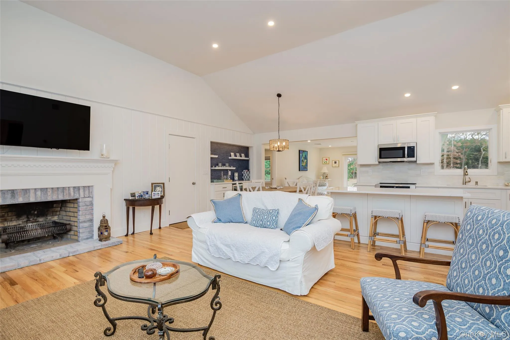 Living room featuring lofted ceiling, a chandelier, light wood-style flooring, recessed lighting, and a brick fireplace Living room featuring lofted ceiling, a chandelier, light wood-style flooring, recessed lighting, and a brick fireplace