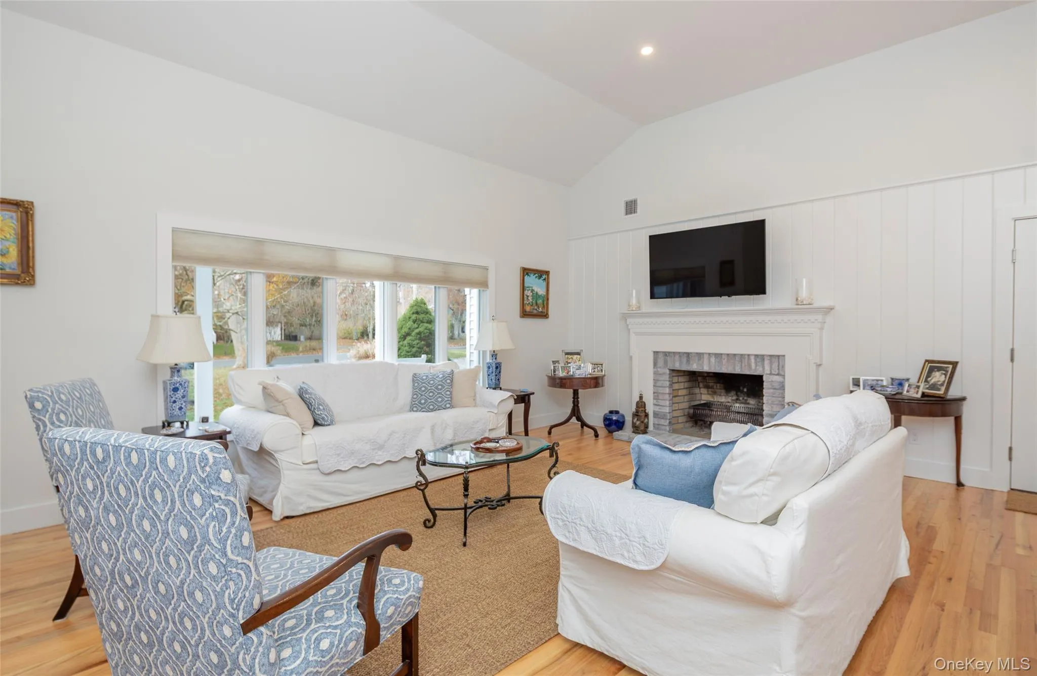 Living area featuring light wood-type flooring, vaulted ceiling, a brick fireplace, and recessed lighting Living area featuring light wood-type flooring, vaulted ceiling, a brick fireplace, and recessed lighting