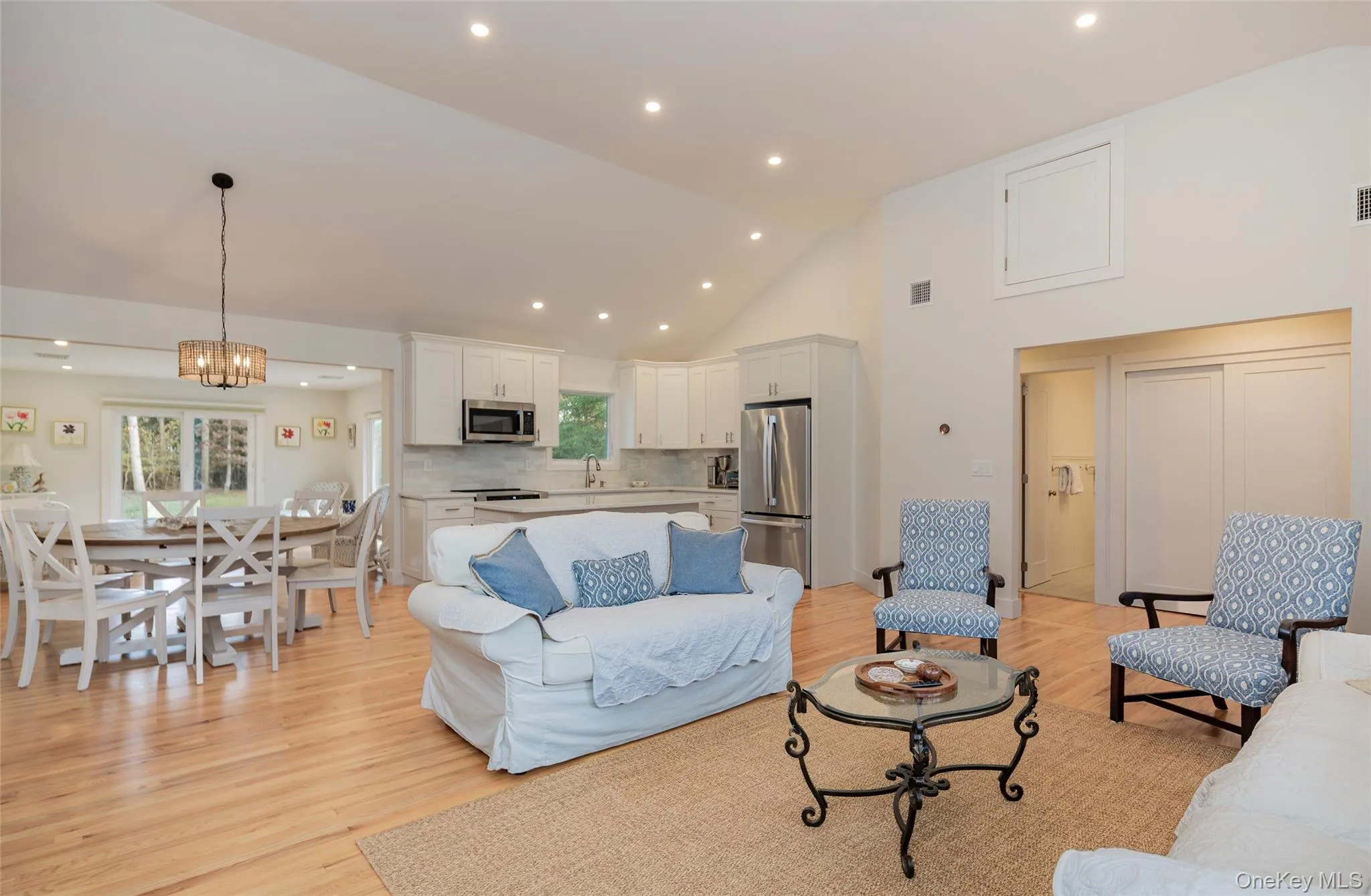Living area with light wood finished floors, high vaulted ceiling, a chandelier, and recessed lighting Living area with light wood finished floors, high vaulted ceiling, a chandelier, and recessed lighting