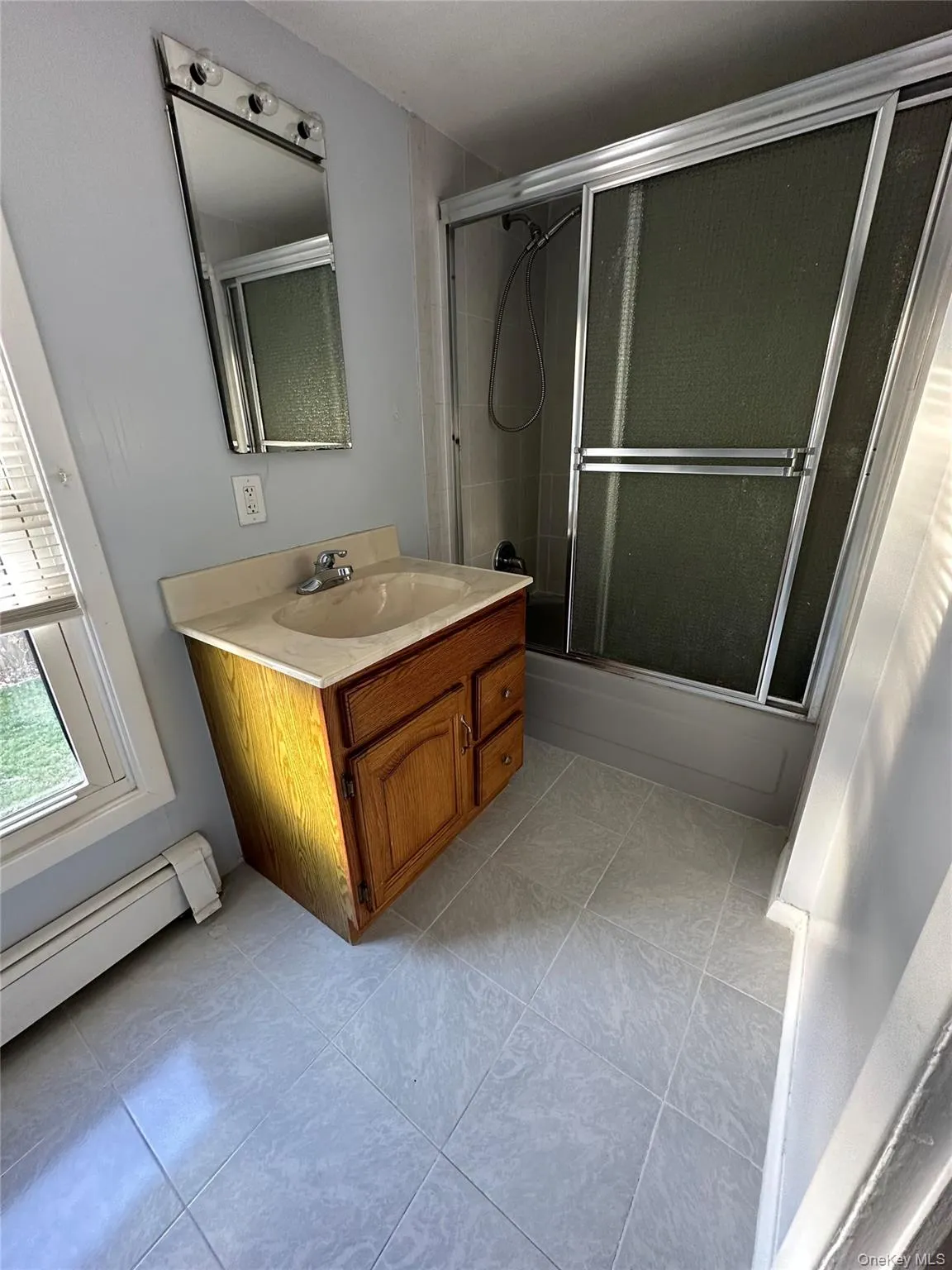 Bathroom featuring bath / shower combo with glass door, a baseboard heating unit, and vanity Bathroom featuring bath / shower combo with glass door, a baseboard heating unit, and vanity