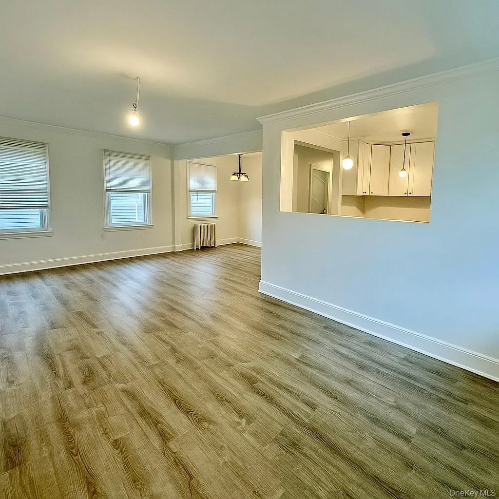 Empty room featuring ornamental molding, wood finished floors, radiator heating unit, and a chandelier Empty room featuring ornamental molding, wood finished floors, radiator heating unit, and a chandelier