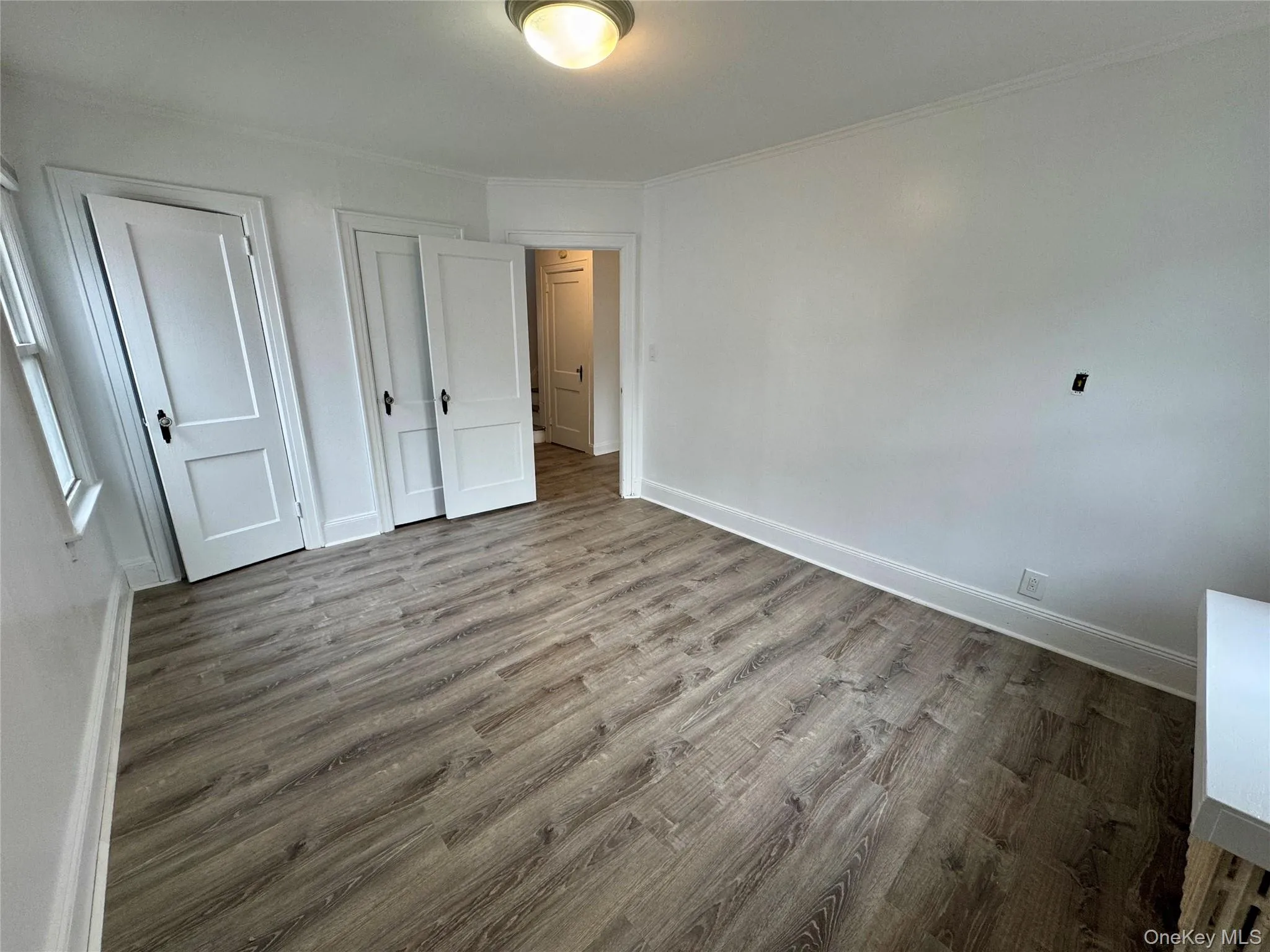 Unfurnished bedroom featuring wood finished floors and ornamental molding Unfurnished bedroom featuring wood finished floors and ornamental molding