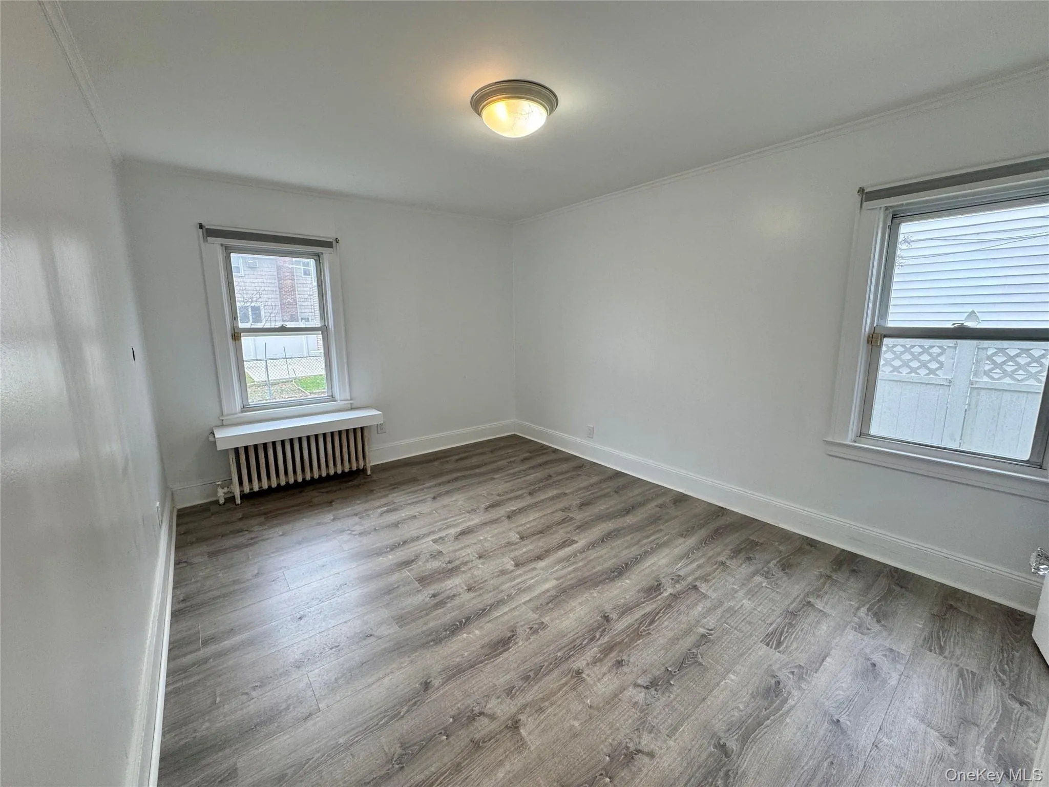 Unfurnished room with light wood finished floors, radiator, and ornamental molding Unfurnished room with light wood finished floors, radiator, and ornamental molding