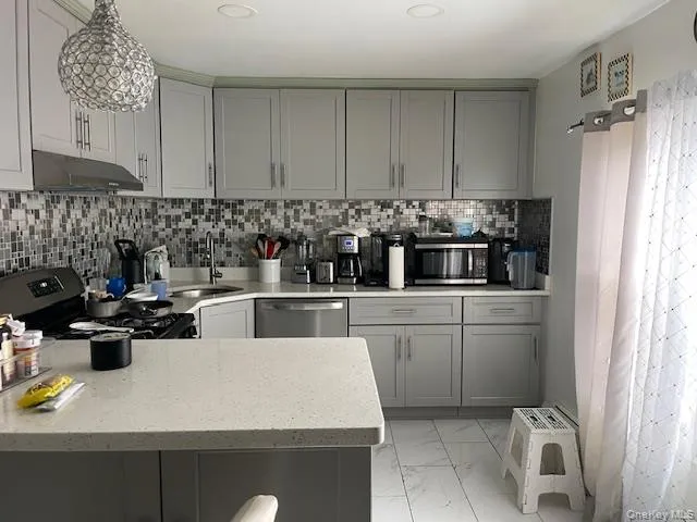 Kitchen featuring gray cabinets, light marble finish flooring, under cabinet range hood, and light stone counters Kitchen featuring gray cabinets, light marble finish flooring, under cabinet range hood, and light stone counters