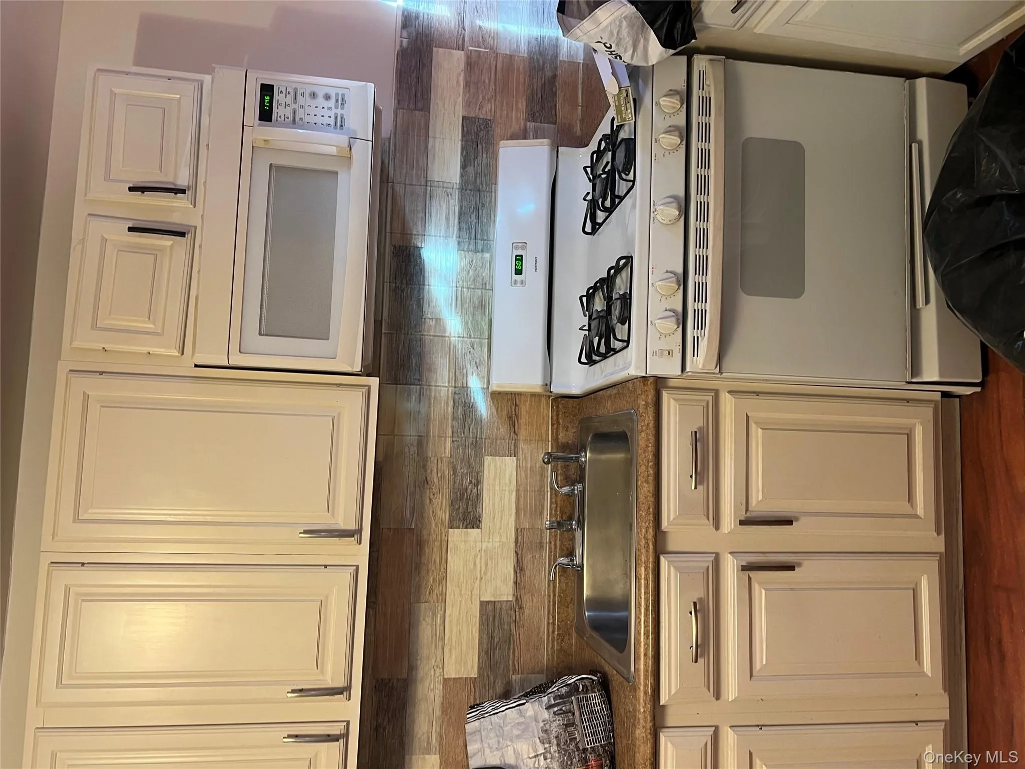 Kitchen with range, white cabinetry, white microwave, dark countertops, and decorative backsplash Kitchen with range, white cabinetry, white microwave, dark countertops, and decorative backsplash