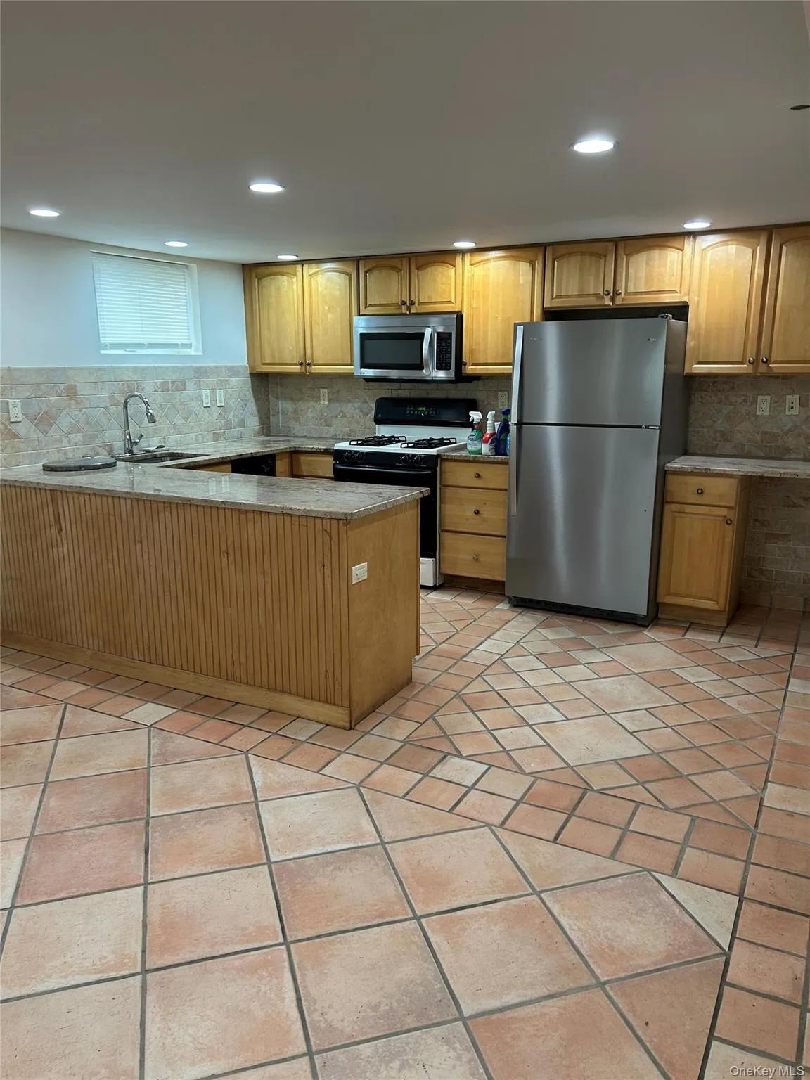 Kitchen with appliances with stainless steel finishes, light stone counters, a peninsula, backsplash, and recessed lighting Kitchen with appliances with stainless steel finishes, light stone counters, a peninsula, backsplash, and recessed lighting