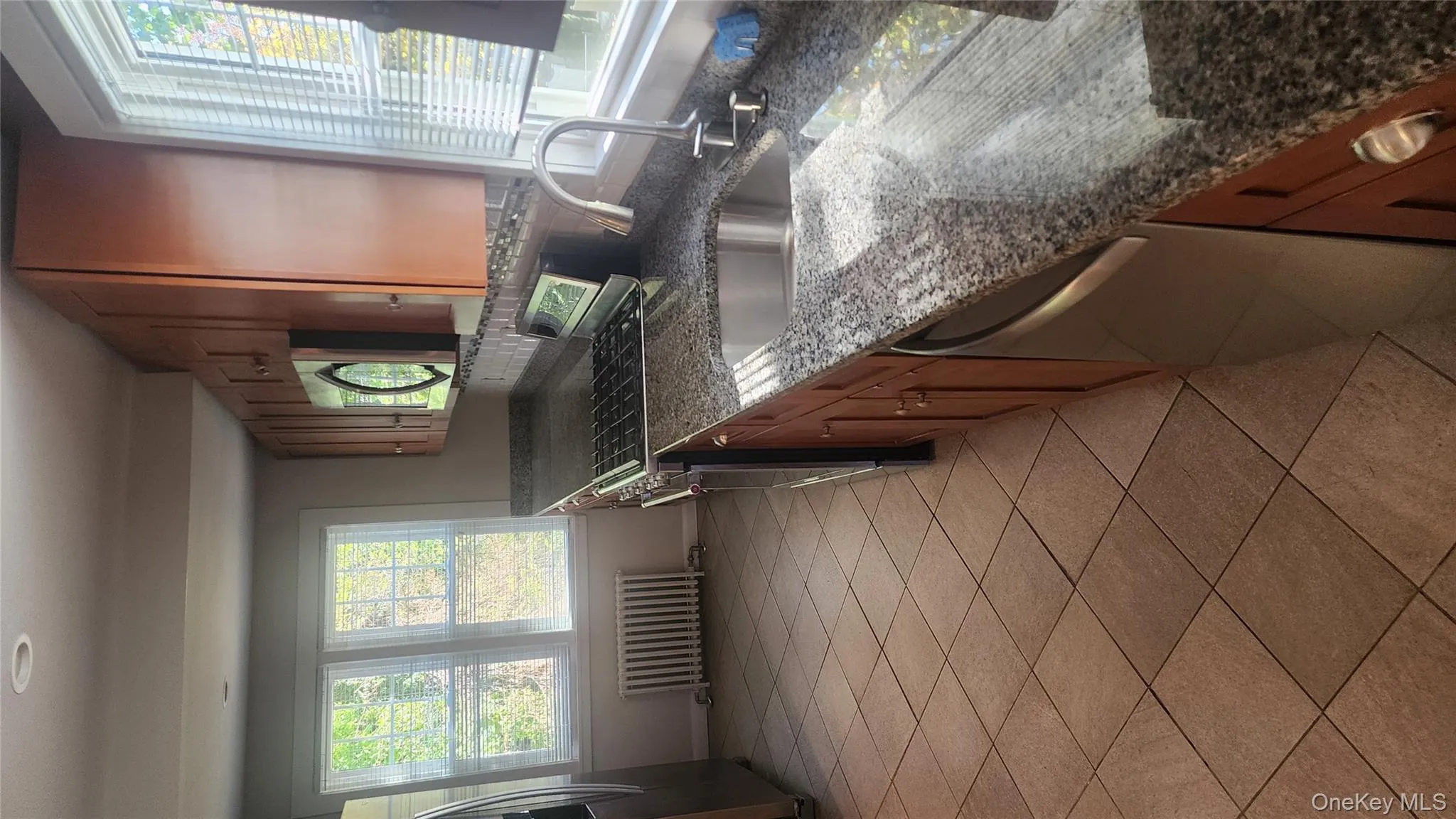 Kitchen featuring brown cabinetry, stainless steel gas stove, dark stone countertops, radiator, and dishwasher Kitchen featuring brown cabinetry, stainless steel gas stove, dark stone countertops, radiator, and dishwasher