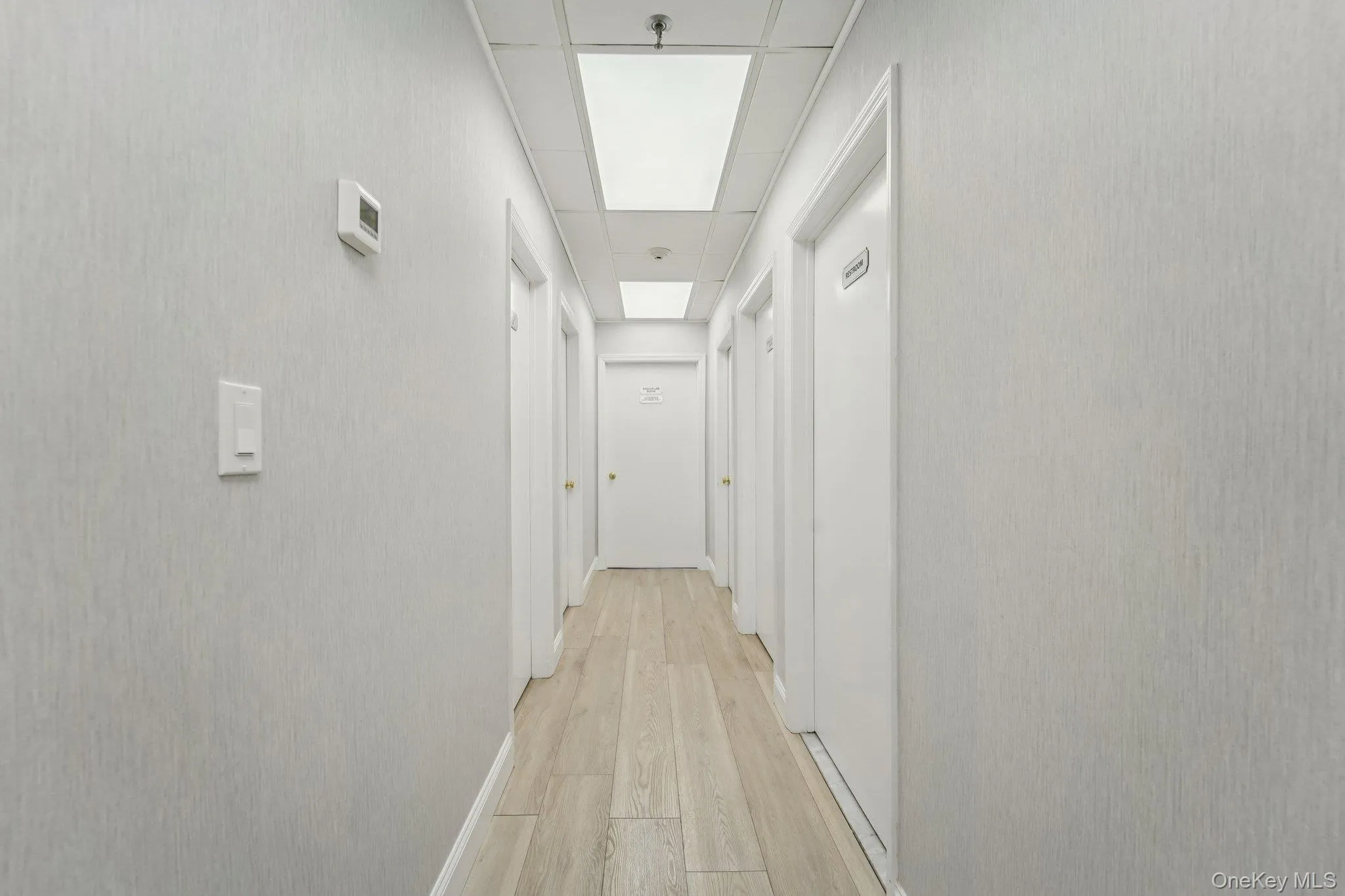 Hallway featuring light wood finished floors and a paneled ceiling Hallway featuring light wood finished floors and a paneled ceiling