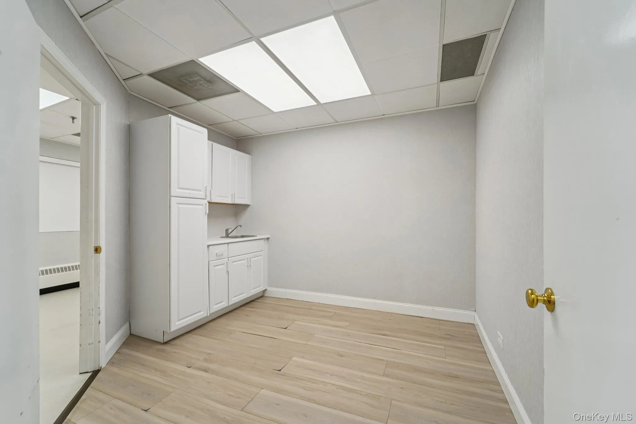 Laundry area featuring a drop ceiling, light wood-type flooring, and a baseboard radiator Laundry area featuring a drop ceiling, light wood-type flooring, and a baseboard radiator