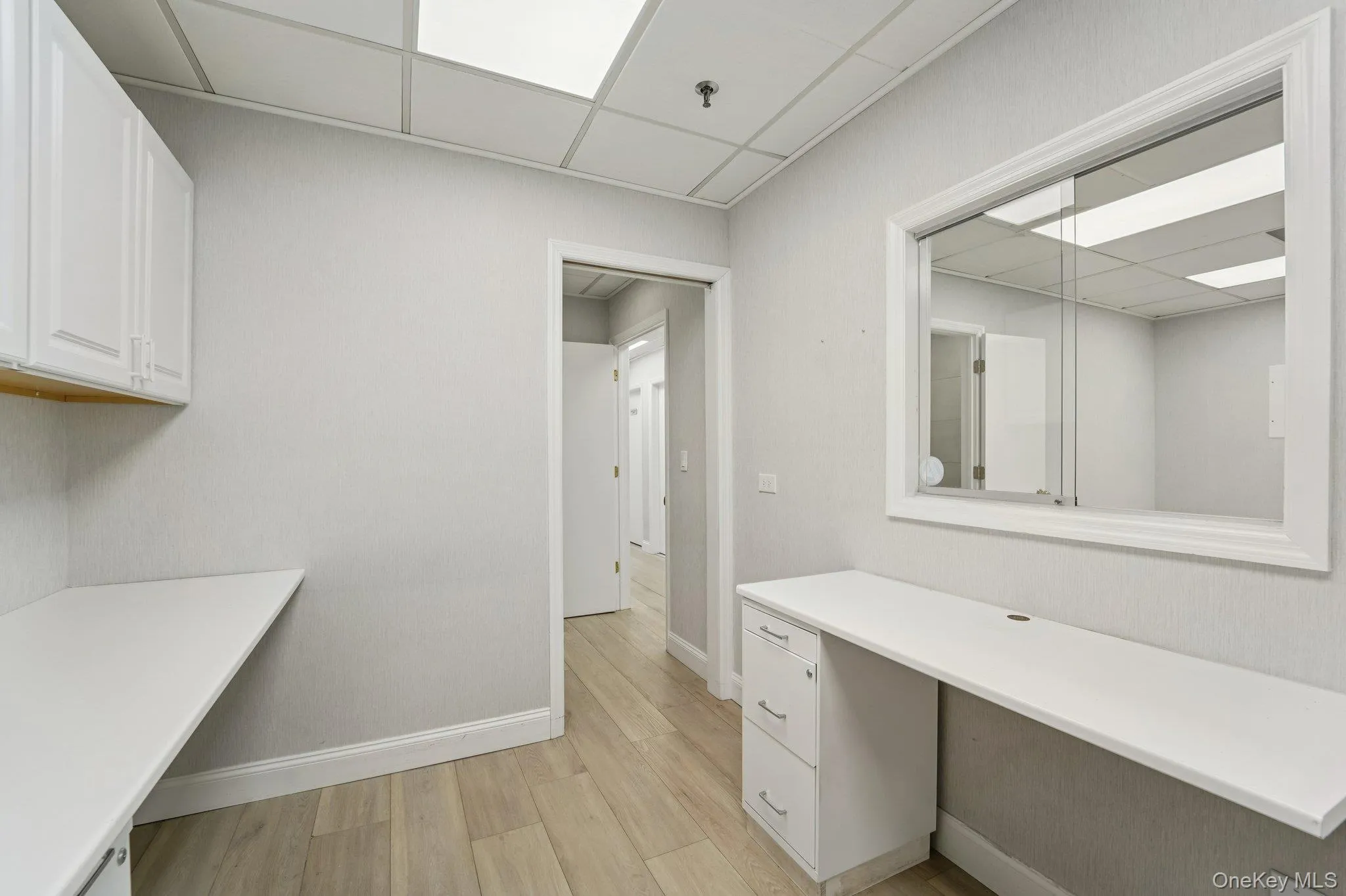 Unfurnished office featuring built in desk, a drop ceiling, and light wood-type flooring Unfurnished office featuring built in desk, a drop ceiling, and light wood-type flooring