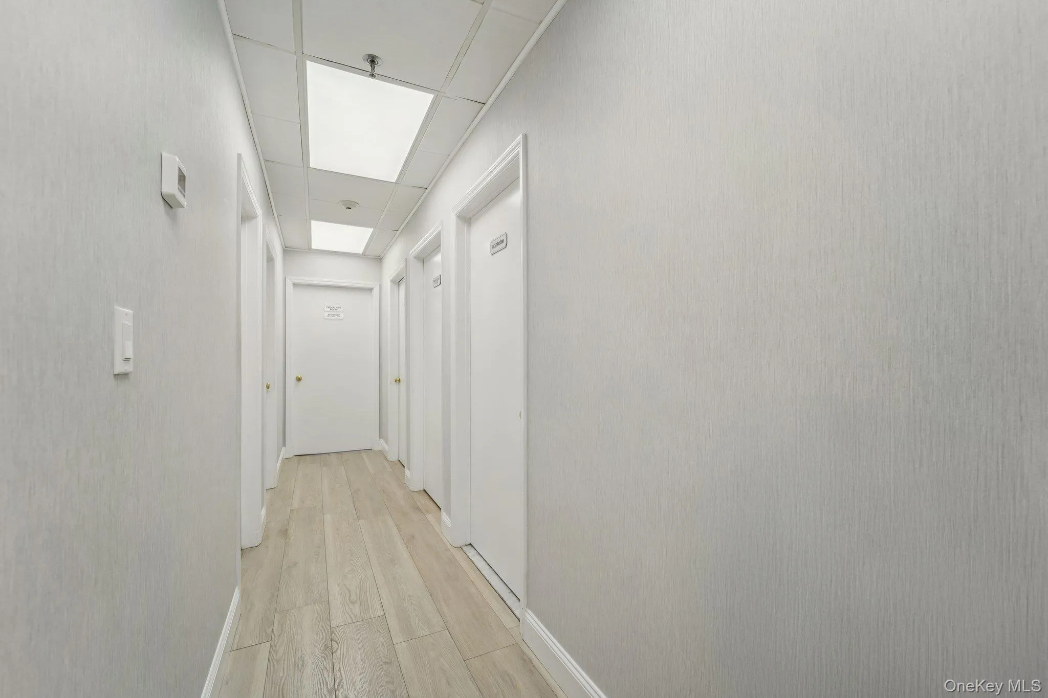 Hallway featuring light wood-type flooring and a paneled ceiling Hallway featuring light wood-type flooring and a paneled ceiling
