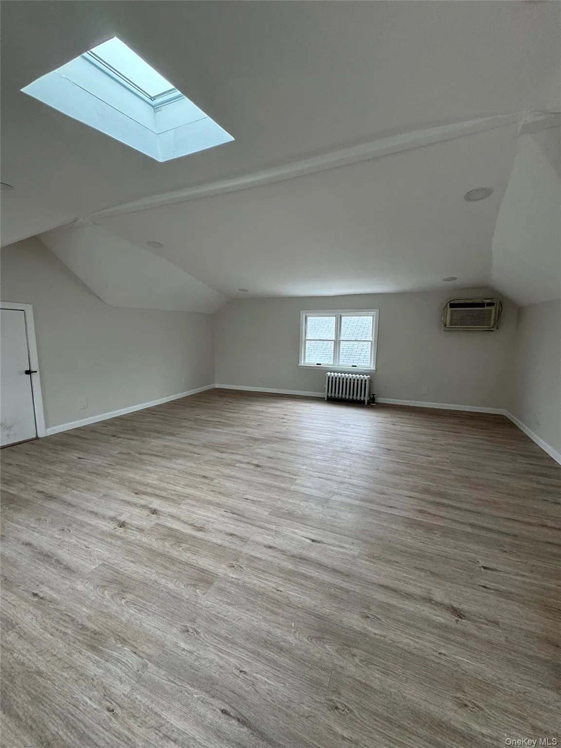 Additional bedroom with lofted ceiling, a skylight, radiator, and light wood-style flooring Additional bedroom with lofted ceiling, a skylight, radiator, and light wood-style flooring